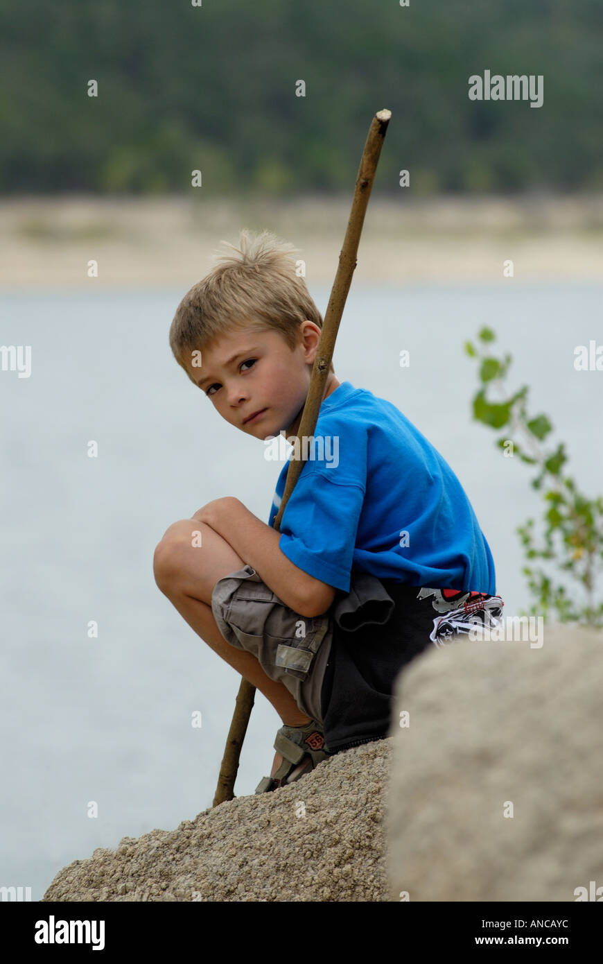 Kleiner Junge sitzt auf einem Felsen mit einem Stock Stockfoto