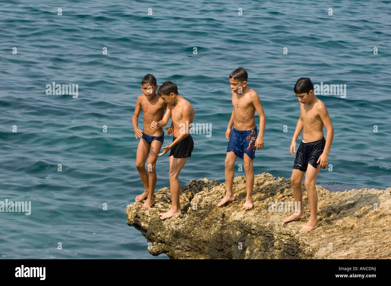 vier Jungs, die auf den Felsen am Meer Stockfoto