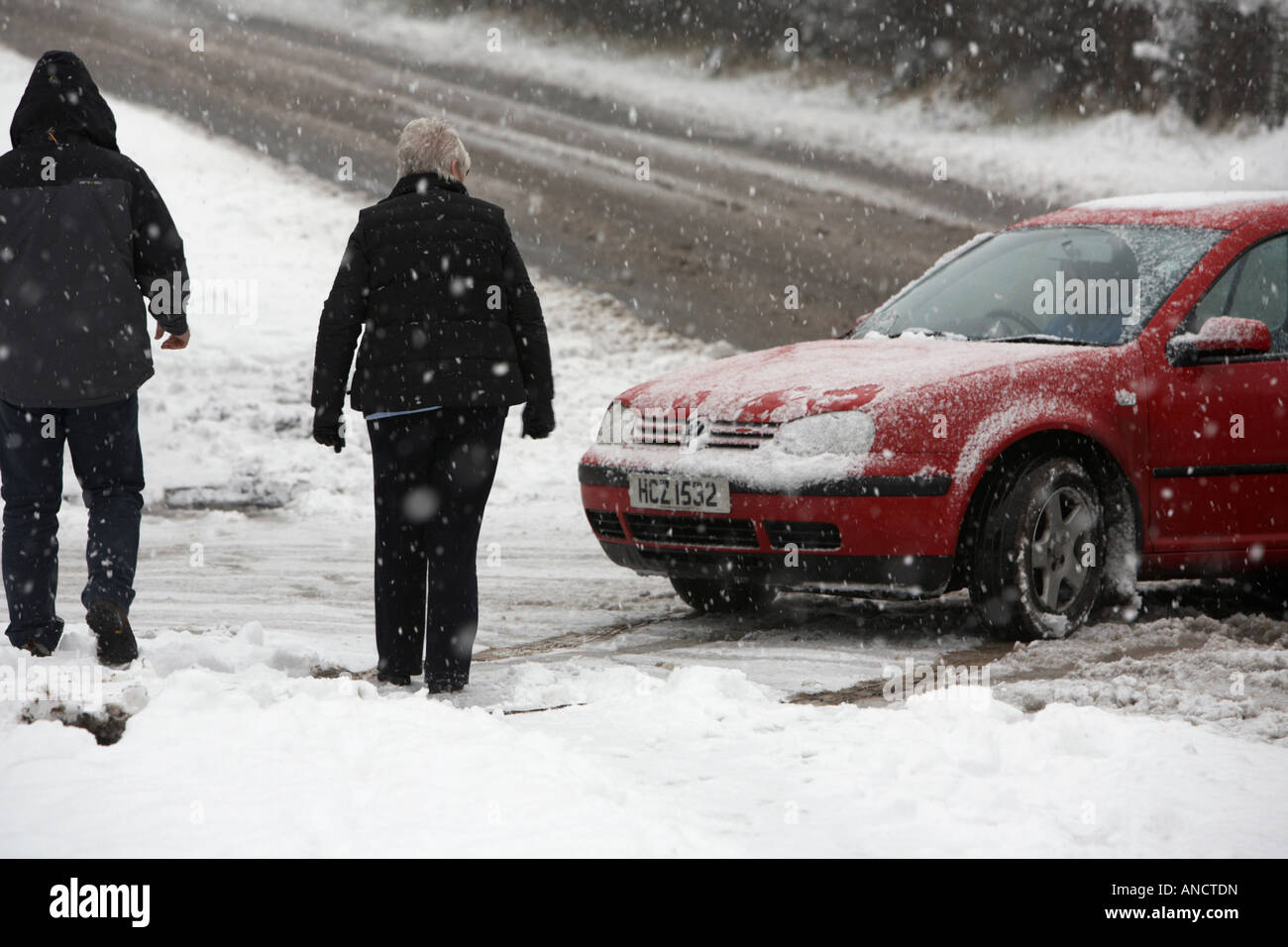 Mann und Frau, die das Auto betrachten Sie haben gerade geholfen, ein Auto zu schieben, das an der Seite der Straße verlassen wurde, die im Schnee stecken blieb, nachdem sie bei schlechtem Wetter geschleifet hatten Stockfoto