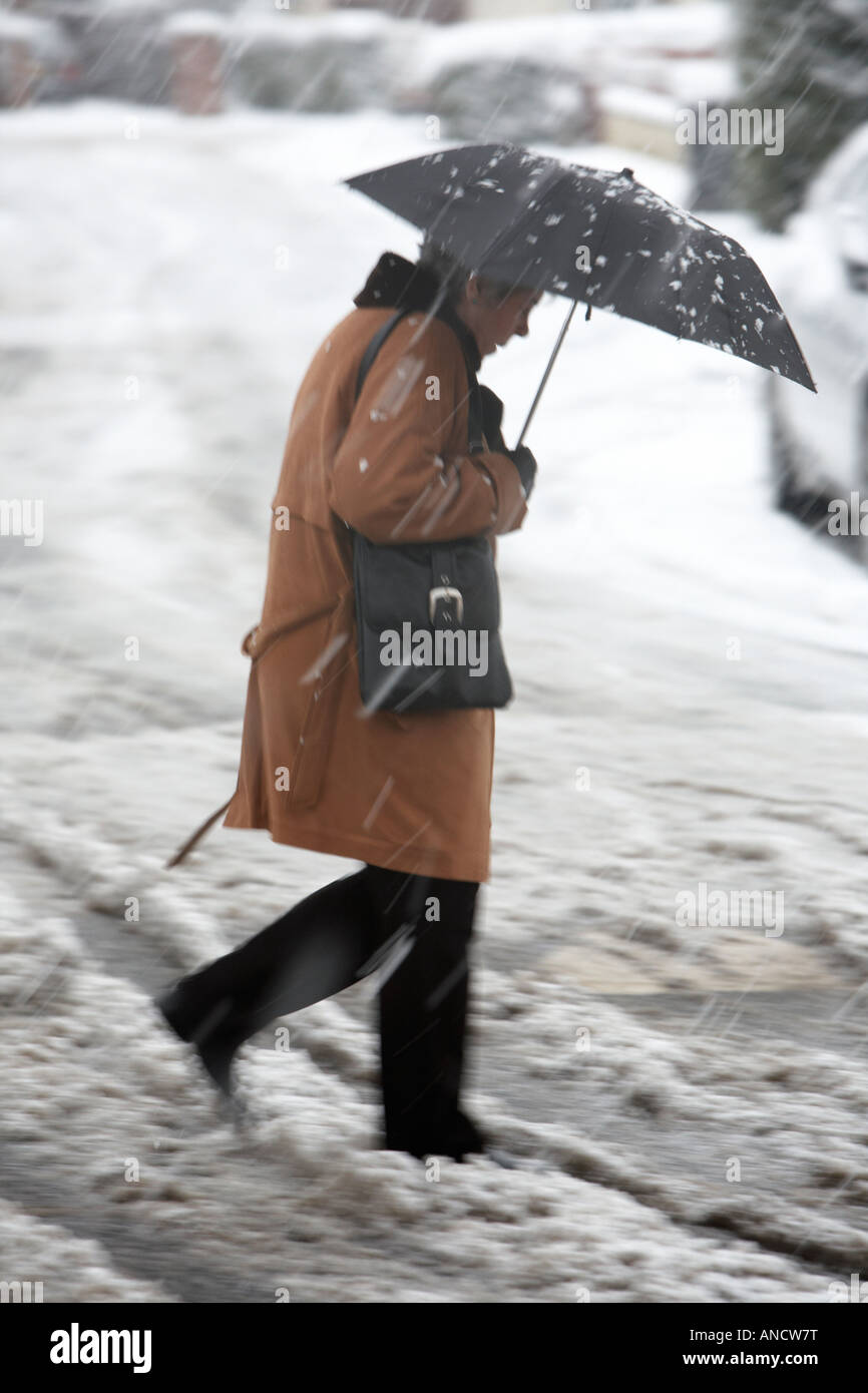 Frau mit Regenschirm geht schnell über schneebedeckte Straße durch Matsch Stockfoto