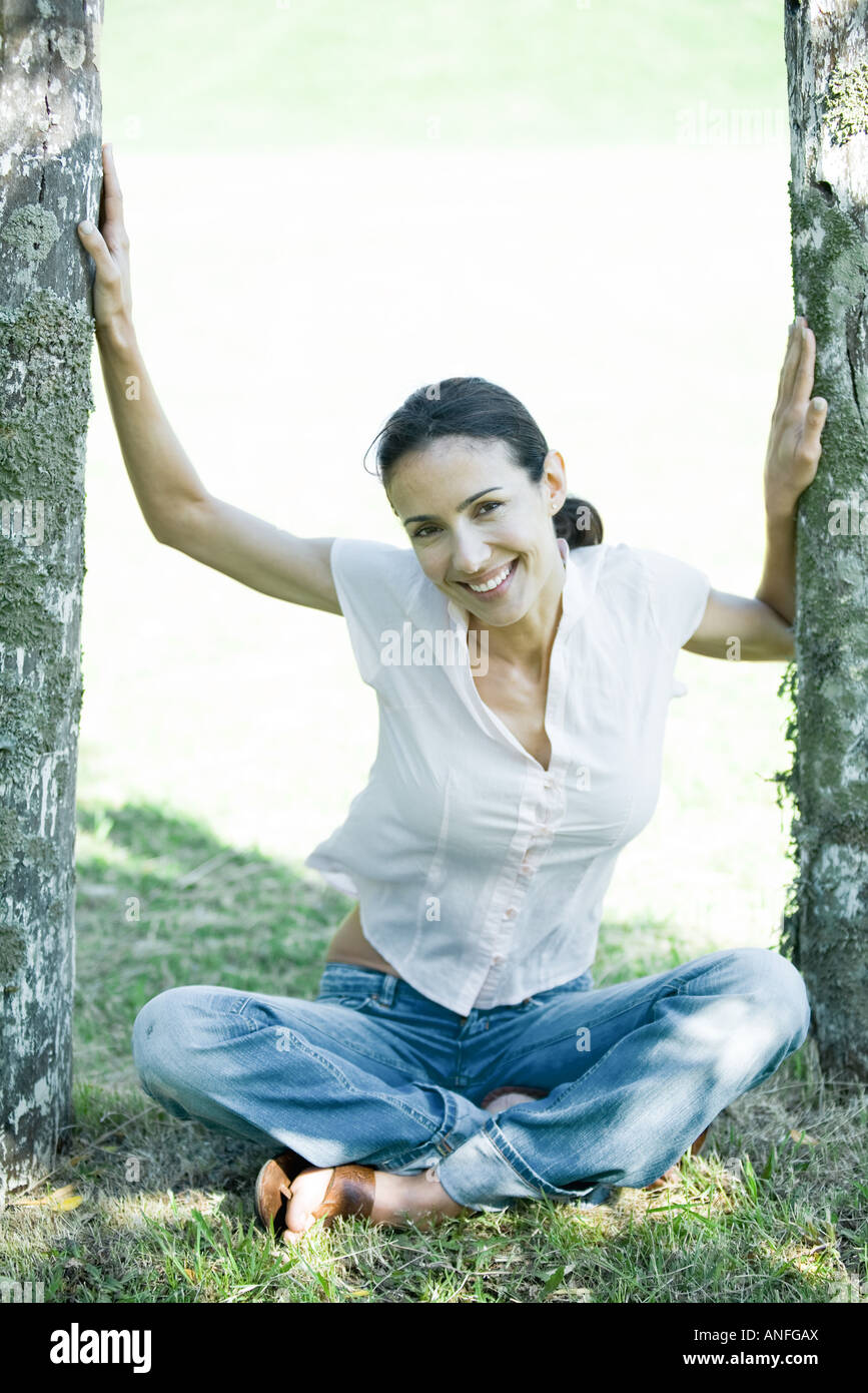 Frau sitzt am Boden zwischen Holzpfosten, lächelnd in die Kamera Stockfoto