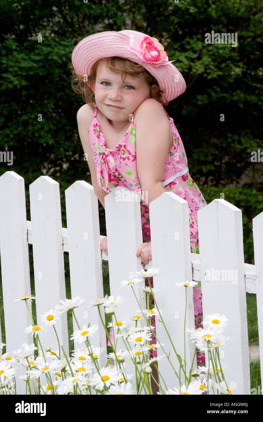 5 Jahre altes Mädchen mit Sommerkleid und Hut stand vor Lattenzaun, Kanada. Stockfoto