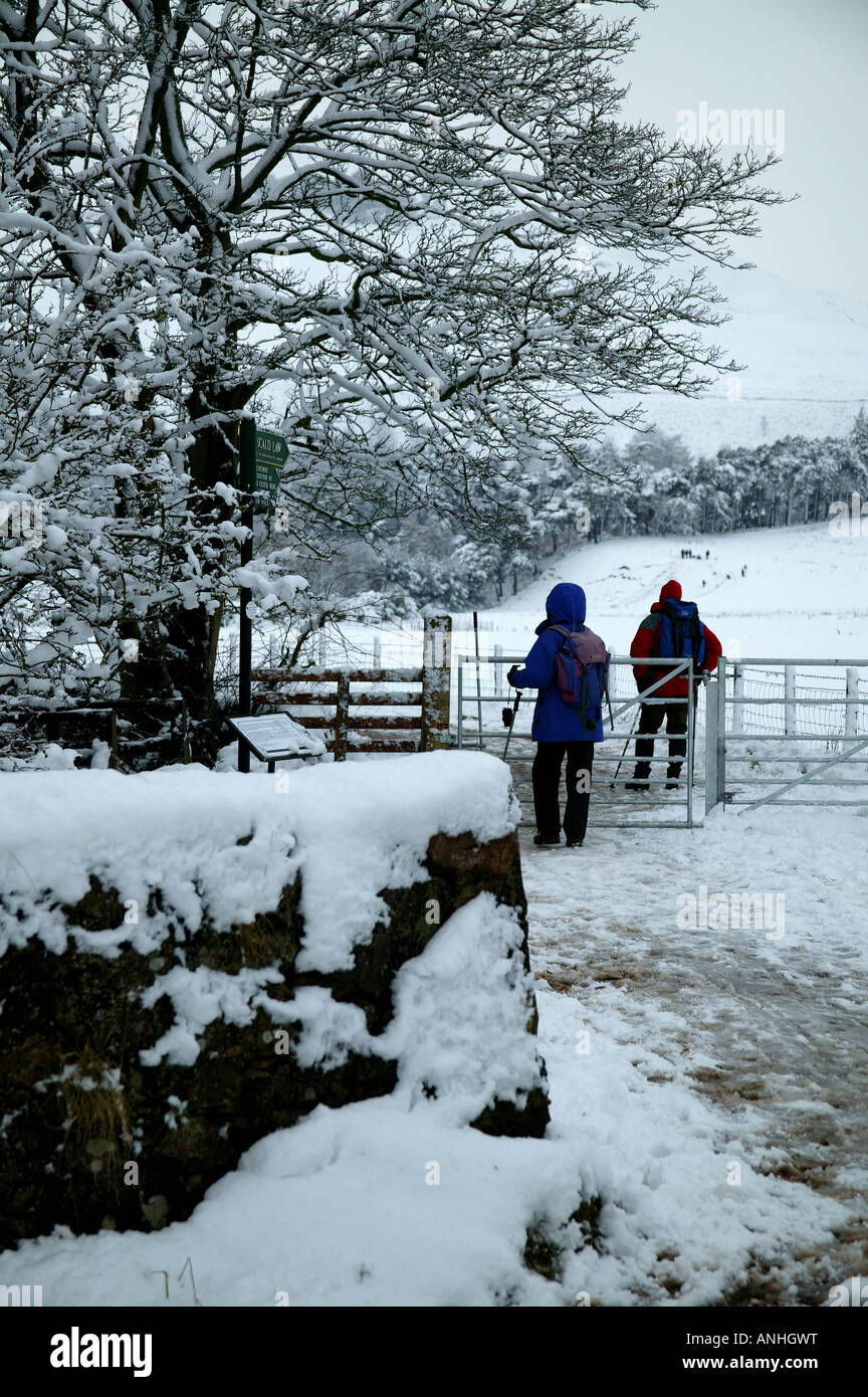 Zwei Wanderer passieren durch ein Tor zu verbrühen Gesetz mit schneebedeckten Bäumen und Wänden auf einem Spaziergang durch Flotterstone Glen, Schottland Stockfoto