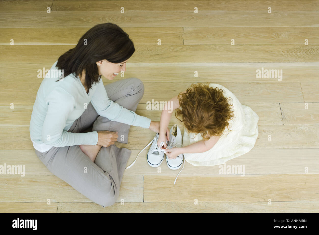 Zeigen Sie Mutter und Mädchen sitzen auf Boden, Mädchen lernen, Schnürsenkel, binden aus direkt über an Stockfoto