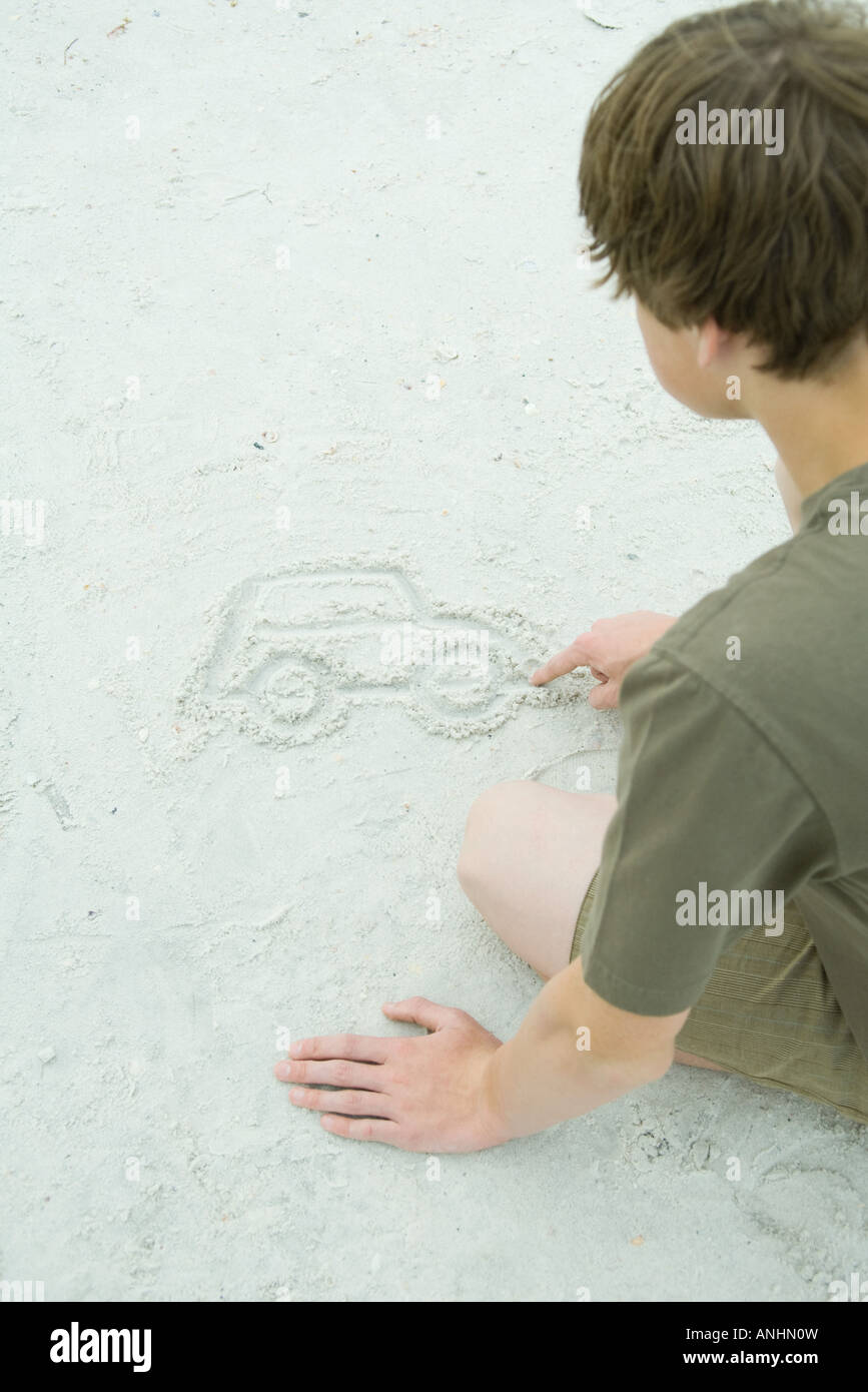 Teenboy zeichnen Auto in sand Stockfoto