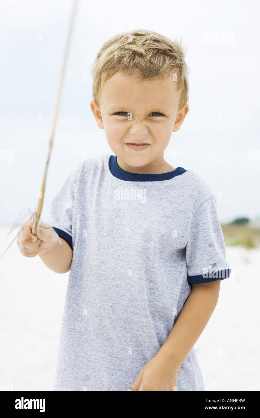 Kleiner Junge hält Stick, Schielen auf Kamera Stockfoto