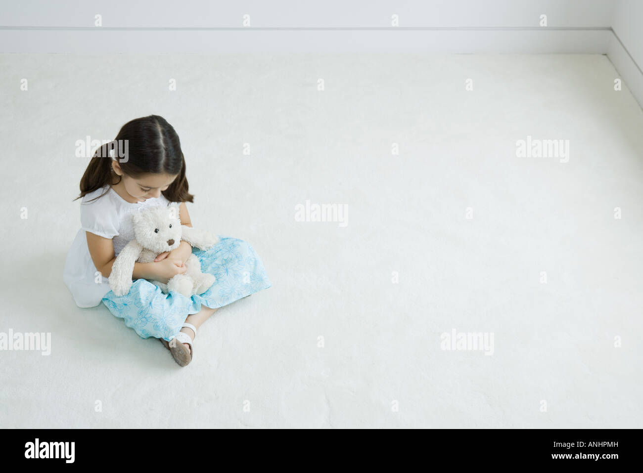 Mädchen sitzen auf dem Boden halten Teddybär auf Schoß, erhöhte Ansicht Stockfoto