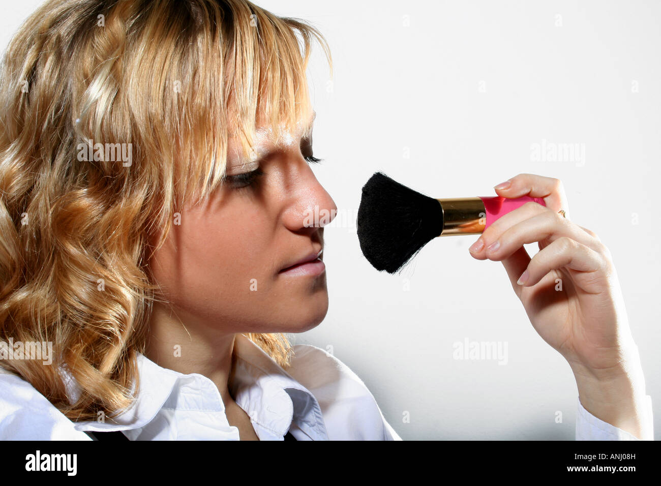 Frau, die Make-up mit einem flauschigen Pinsel aufträgt, sich auf ihr Gesicht mit einem neutralen Hintergrund fokussiert, zeigt eine Schönheitsroutine. Stockfoto