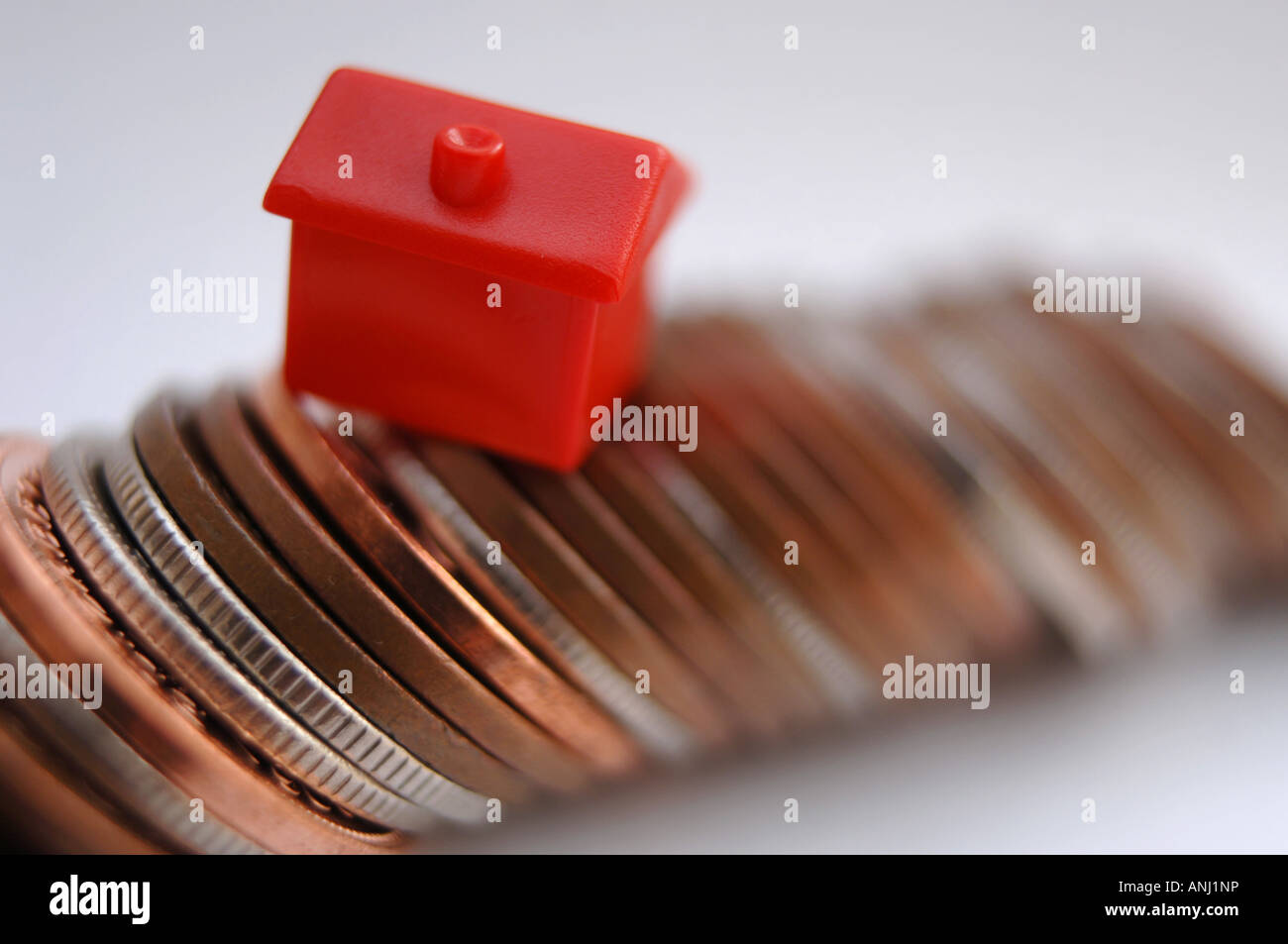Eine rote Monolopy Haus stehen auf einem Haufen Münzen, Immobilienpreise, Darlehen und Hypotheken zu illustrieren Stockfoto