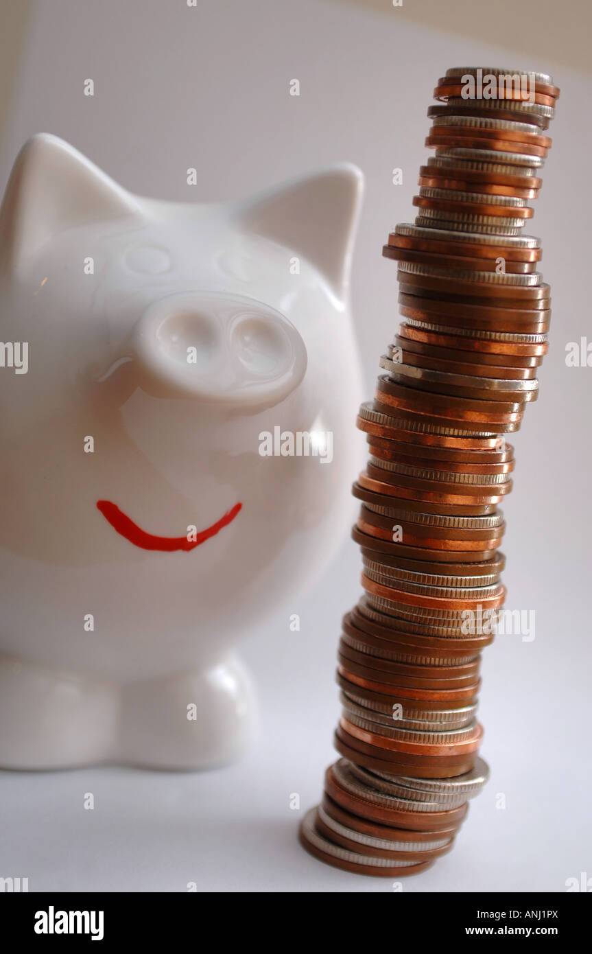 Ein glücklich aussehende Sparschwein steht neben einem Stapel Münzen um Einsparungen und erfolgreiches Banking zu illustrieren Stockfoto