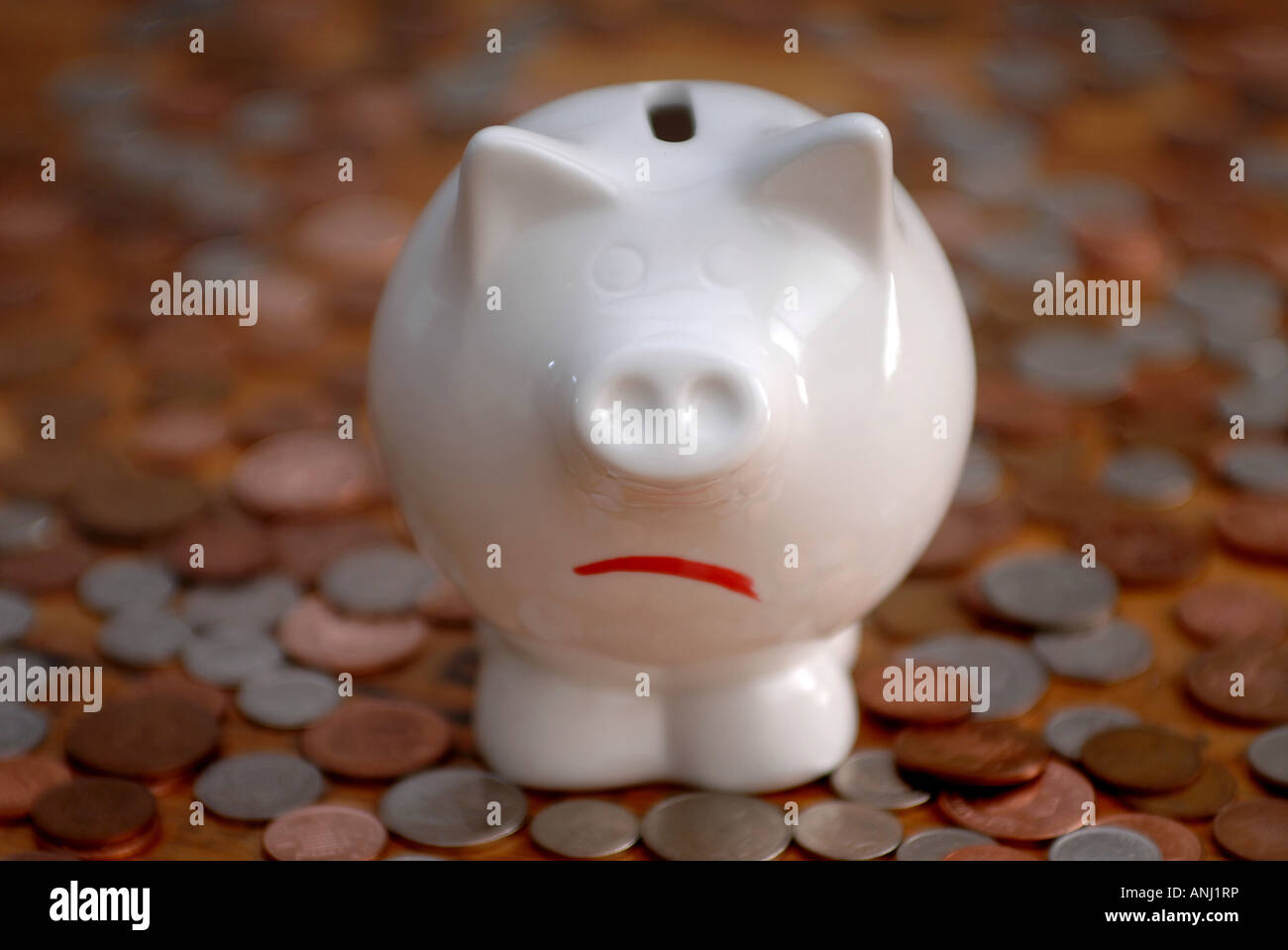 Ein unglücklich Sparschwein steht auf Münzen um Einsparungen und Schulden zu illustrieren. Stockfoto