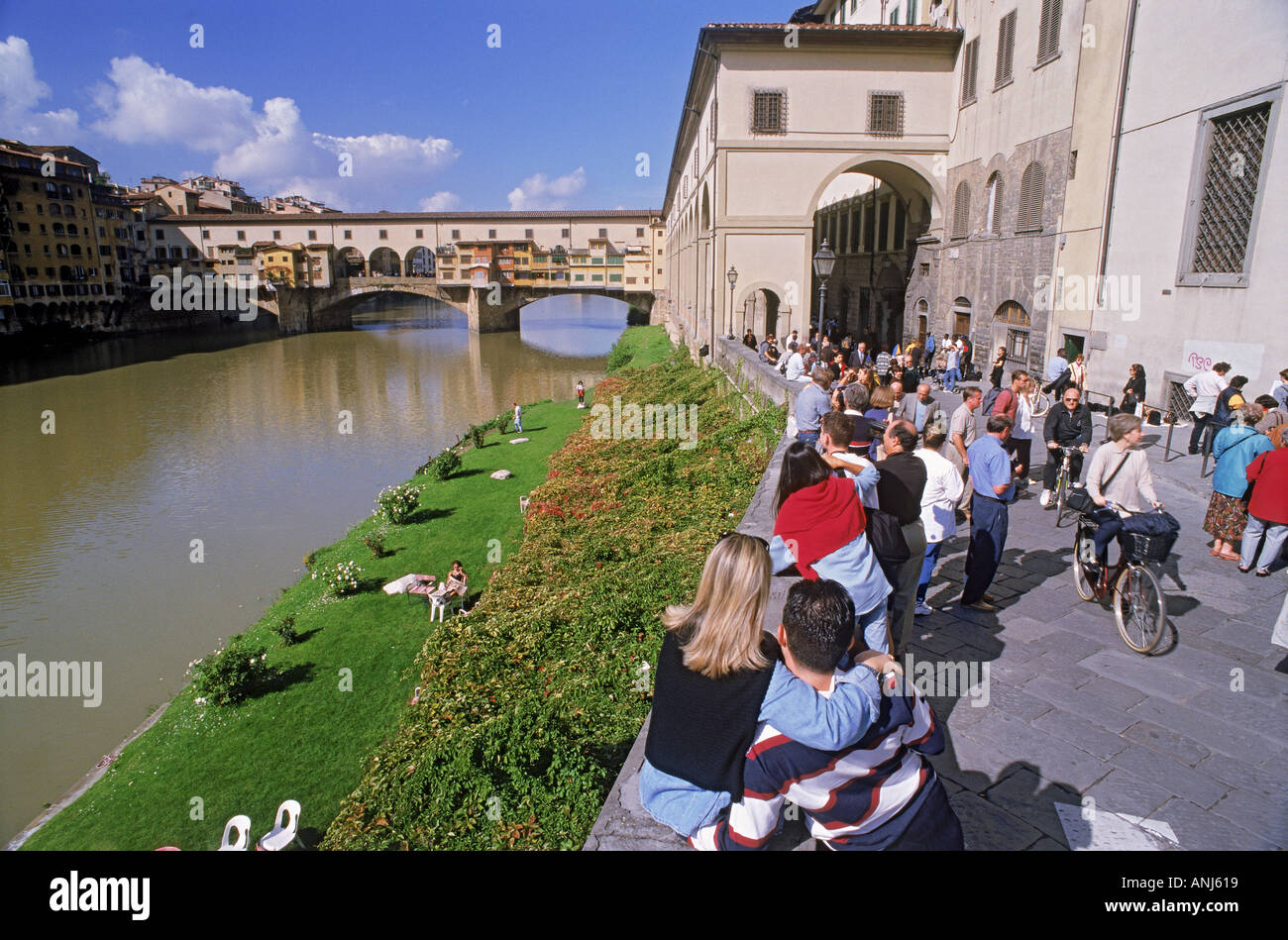 Menschen zu Fuß, in der Nähe von Radfahren und auf Mauer sitzend Uffizi Galerie am Fluss Arno in Florenz Stockfoto