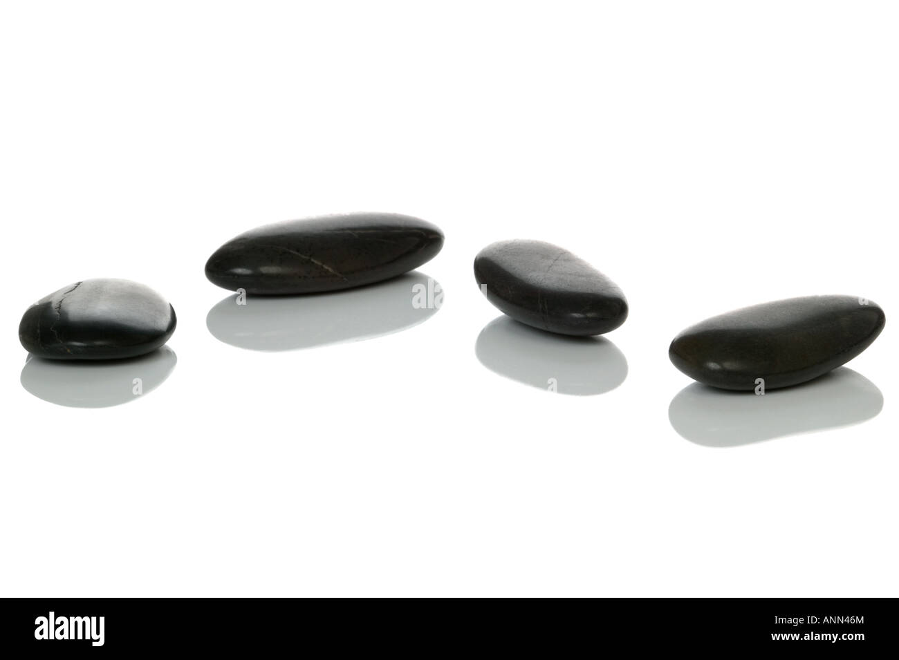 Vier schwarze Kieselsteine mit Reflexionen auf einer weißen Fläche Stockfoto