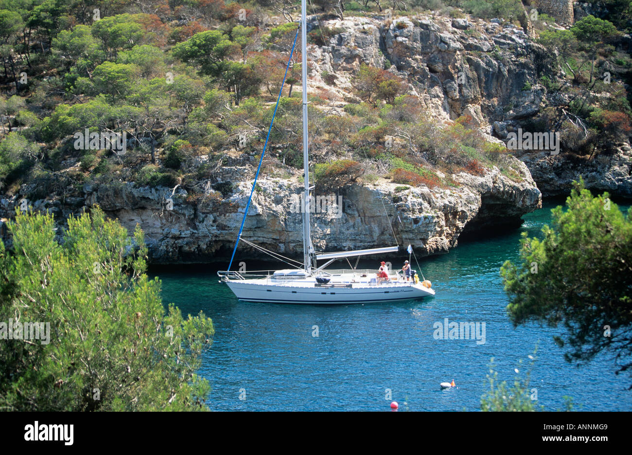 Eine Yacht, der seinen Weg in einer engen Bucht am Fuße des Baumes felsigen Klippen in der Nähe von Hafen von Cala Figuera besetzt Stockfoto