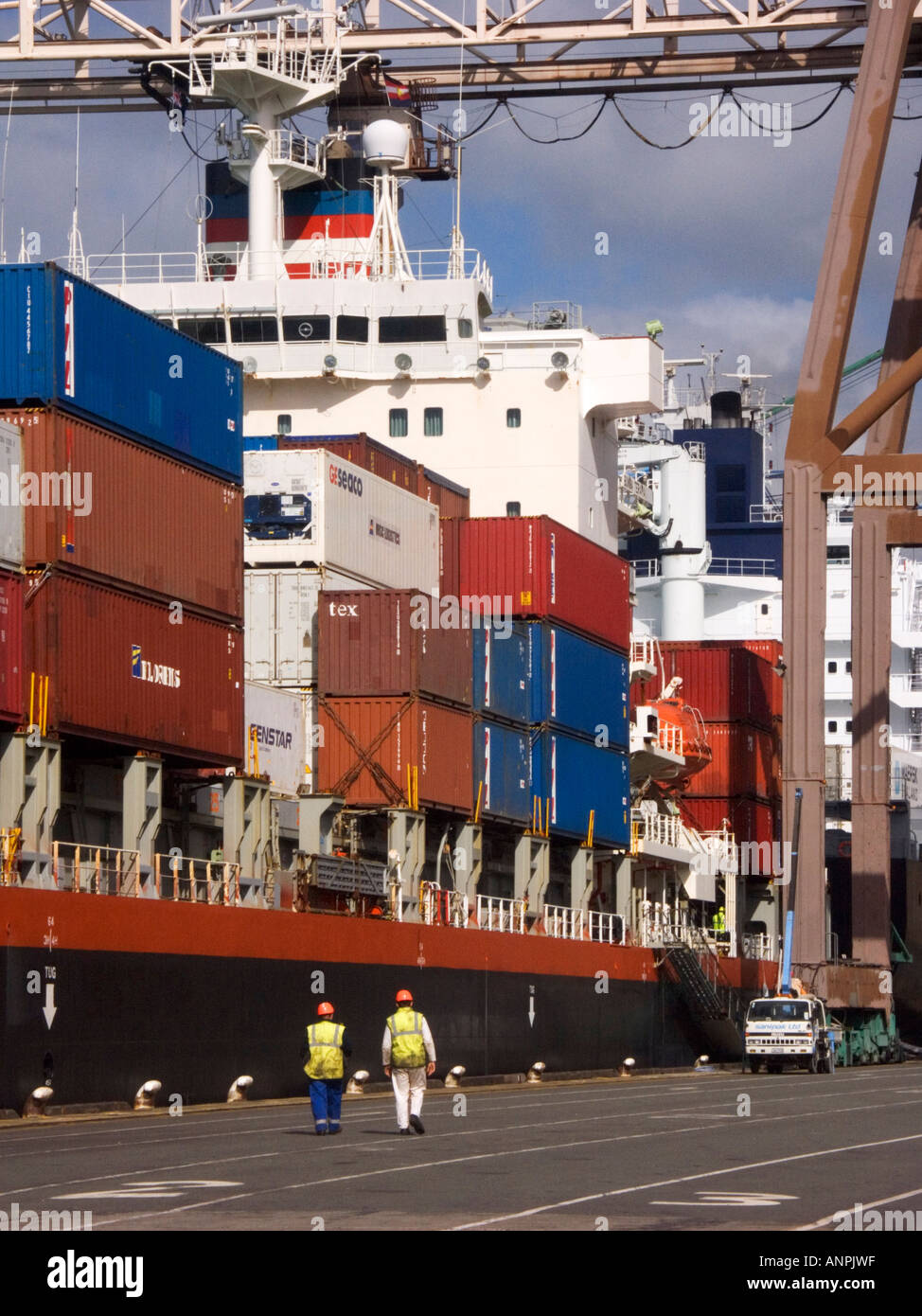 Container auf einem Schiff in Lyttelton, Neuseeland stapeln, wie Hafenarbeiter zum Schiff gehen Stockfoto