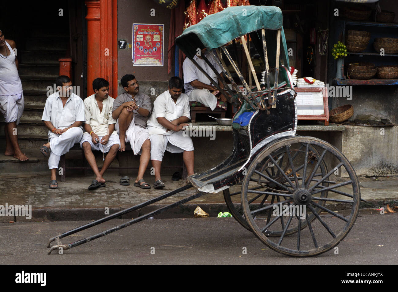 Eine Rikscha steht auf einer der Straßen in der Nähe von Kali Ghat in Kolkata, Indien. Die Rikscha-Puller sitzen in der Nähe, Tee zu trinken. Stockfoto