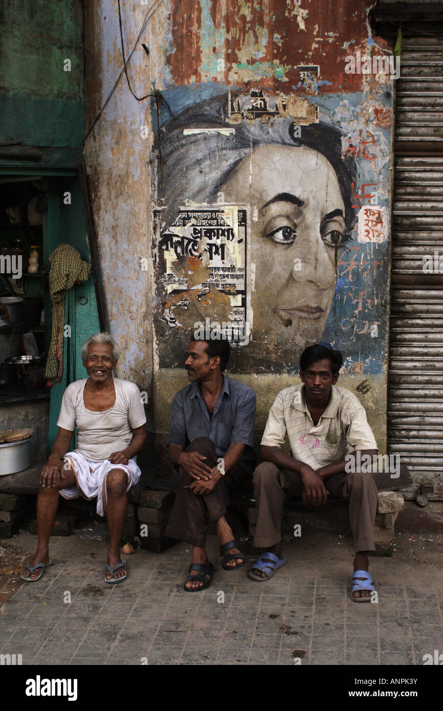 Männer in Kalkutta sitzen unter einer bemalten Wand Zeichen, das zeigt der späten Premierminister von Indien, Indira Gandhi. Stockfoto