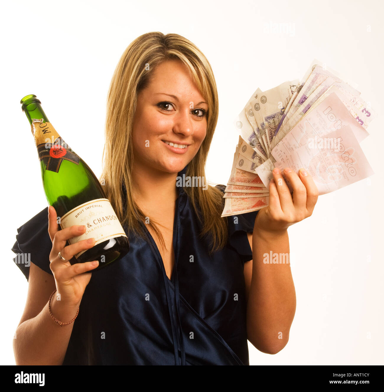 junge blonde Frau Lotto-Gewinner mit einer Fistfull von Bargeld und eine Flasche Champagner Stockfoto