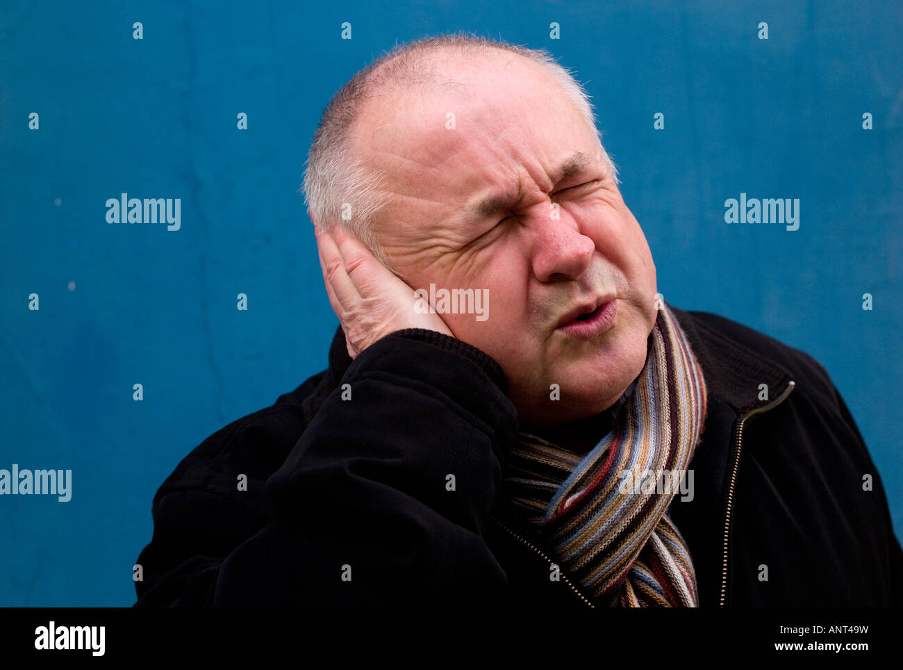 Mann mittleren Alters Glatzenbildung trägt einen Schal - zuckte vor Schmerz, als er sein Ohr mit seiner Hand Tassen - Ohrenschmerzen leiden Stockfoto