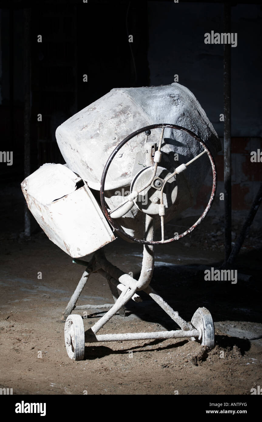 Alte, verwitterte Betonmischmaschine auf einer Baustelle, beleuchtet in einer schwach beleuchteten Industrieumgebung. Stockfoto