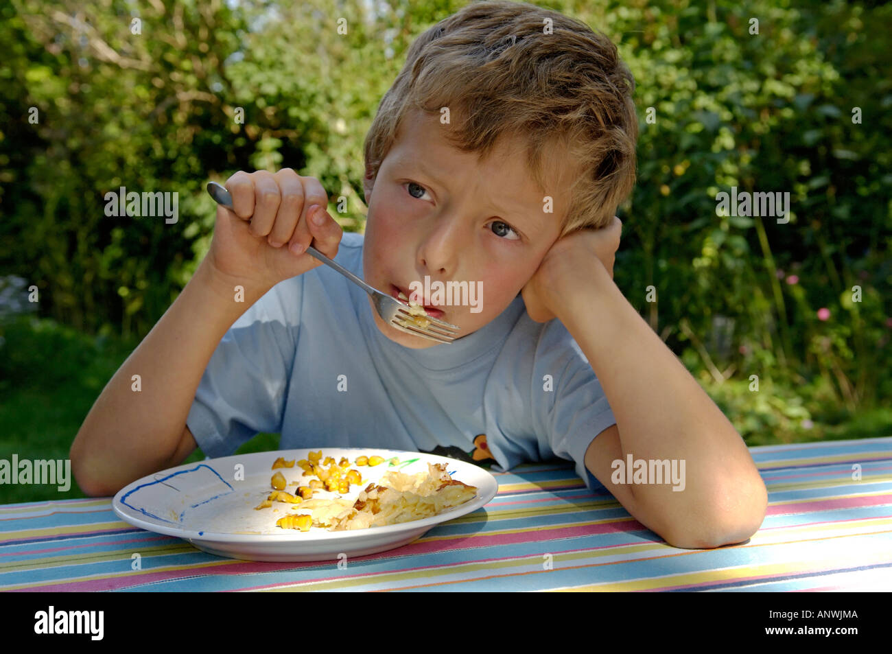 Junge, neun-jährige. ist verträumt sein Essen mit Mais Stockfoto