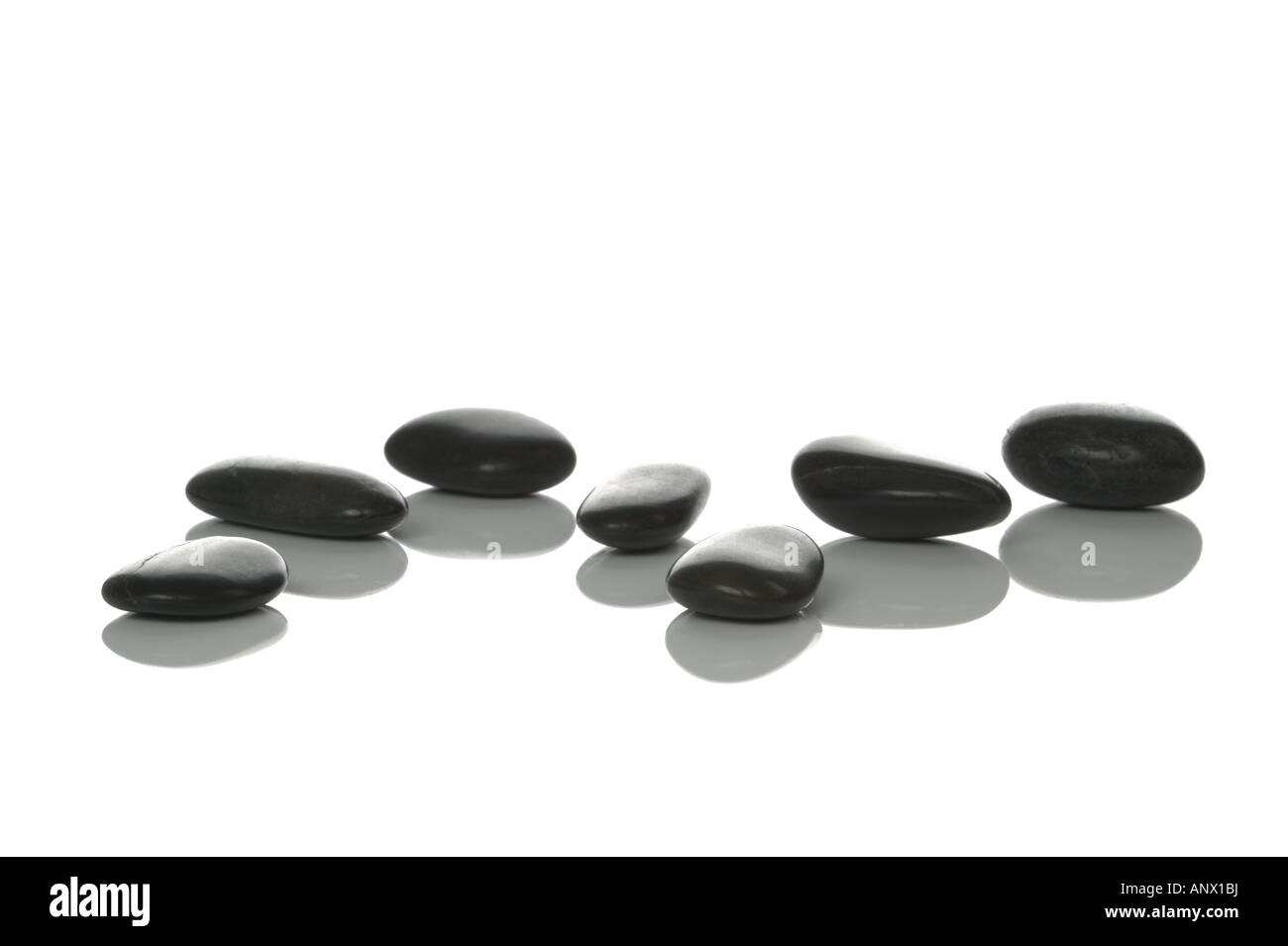 Sieben schwarze Kieselsteine mit Reflexionen auf einem weißen Hintergrund hohe Schlüssel gedreht Stockfoto