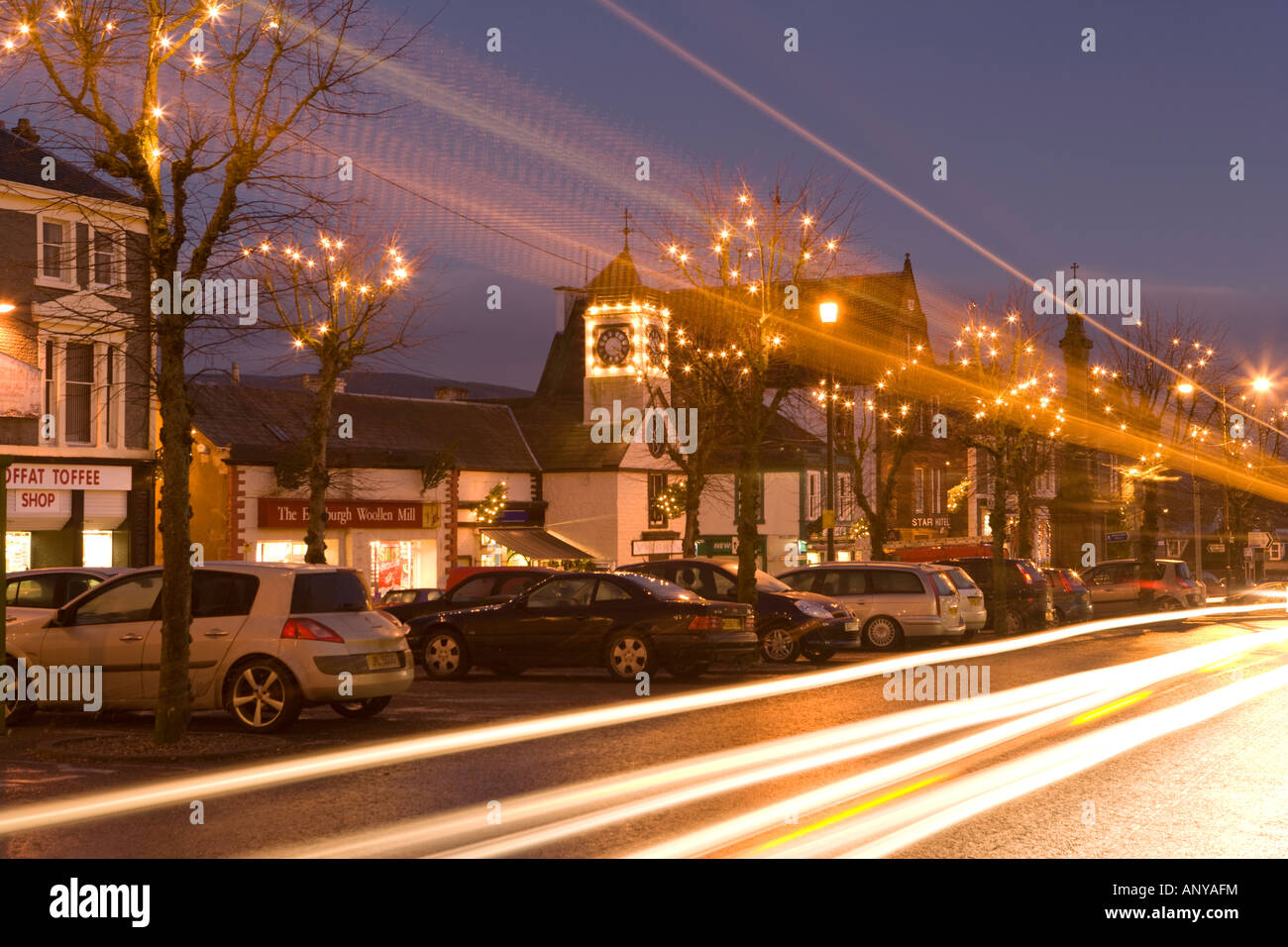 Abenddämmerung Weihnachtsbeleuchtung auf den Bäumen auf der High Street Moffat mit den Lichtspuren der Verkehr schneller vorbei an Schottland, Vereinigtes Königreich Stockfoto