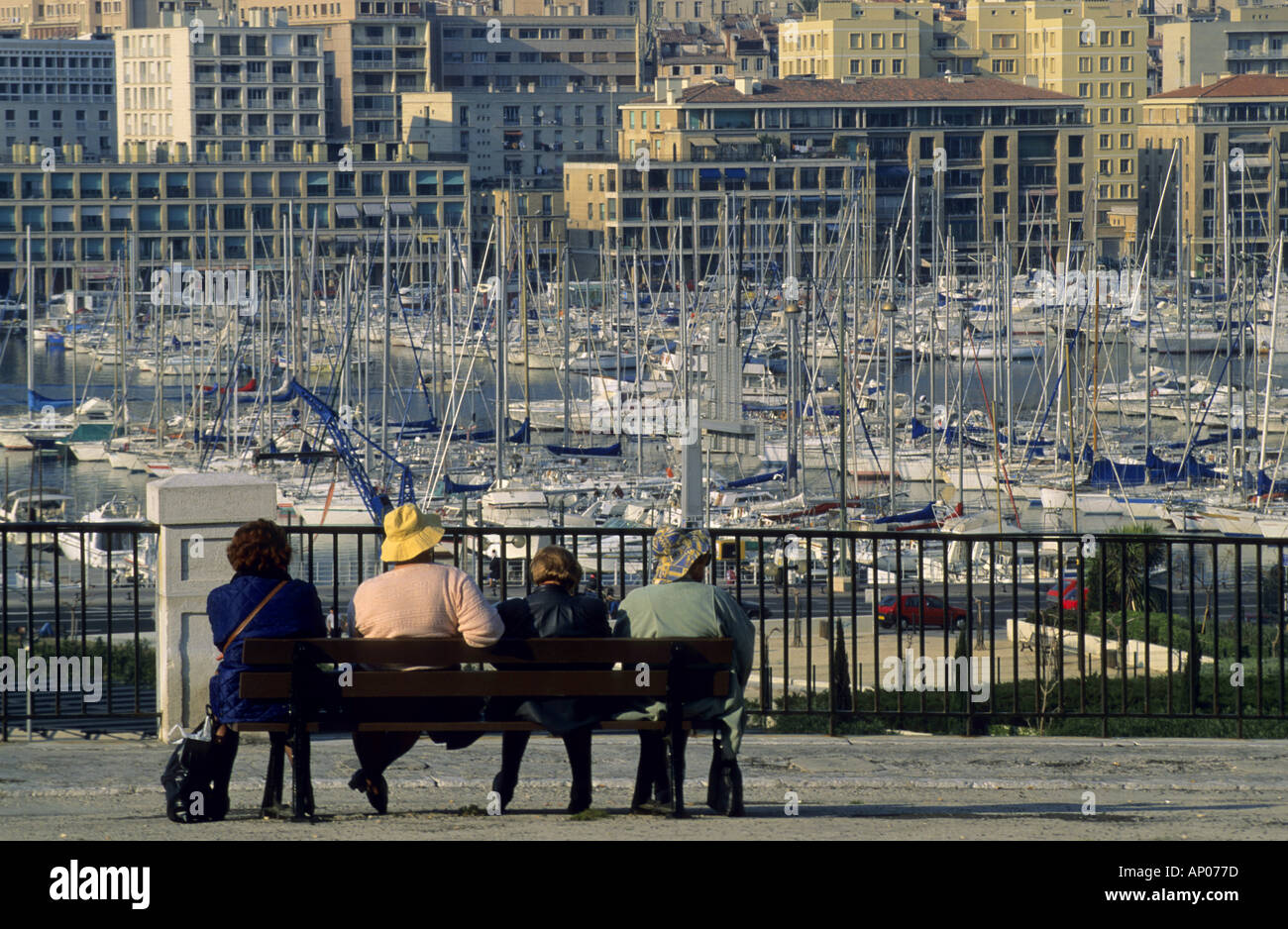 Vier Frauen / Touristen sitzen auf einer Bank in der Sonne mit Blick auf den alten Hafen Marina und seine Boote Stockfoto