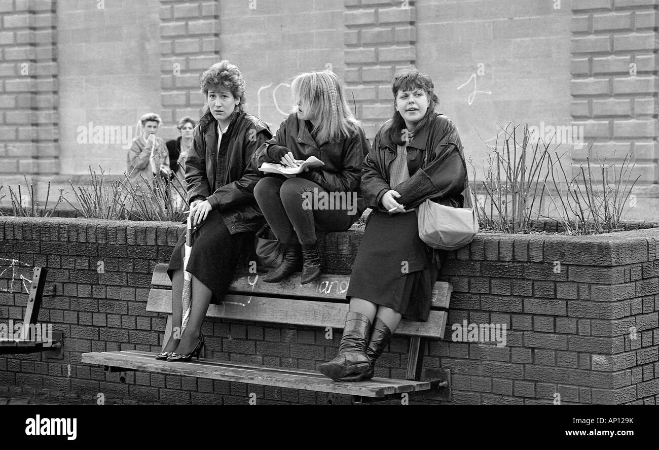Drei Mädchen sitzen im Freien in der Straße in kaltem Wetter rauchen Zigaretten. Stockfoto