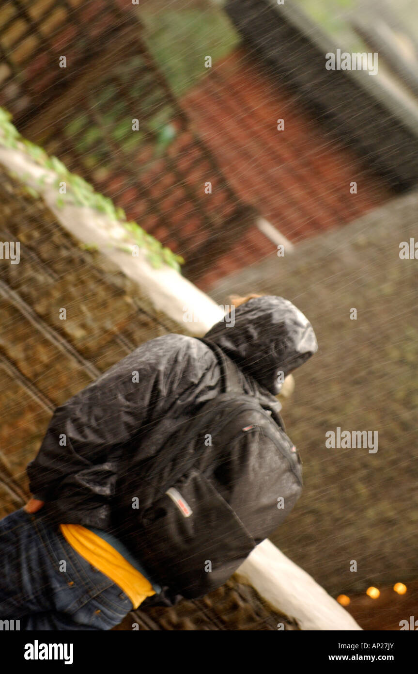 Mann zu Fuß in den Regen tragen eine wasserdichte Jacke und Rucksack mit Kapuze Stockfoto