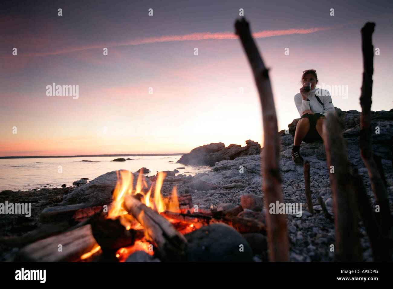 Frau trinkt Wein in der Nähe von einem Kamin am Strand bei Sonnenuntergang, Sysne, Gotland, Schweden Stockfoto