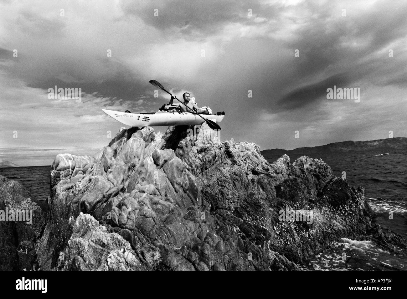 Kajakfahrer Posen in seinem Kajak auf einem Felsen mitten im Meer mit einem Sturm droht in der Ferne Stockfoto