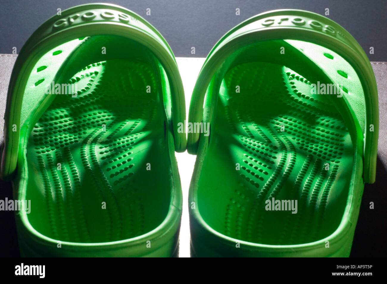 Ein paar helle grüne Crocs clogs mit Licht, das durch das Muster der Bohrungen in das Oberteil Stockfoto