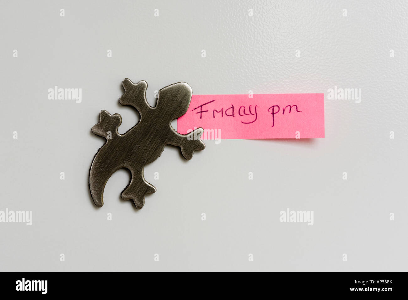 Nahaufnahme von Alligator geformte Edelstahl-Kühlschrank-Magnet auf weißen Kühlschranktür hält Rosa Hinweis sagen: Freitag 19:00 Stockfoto
