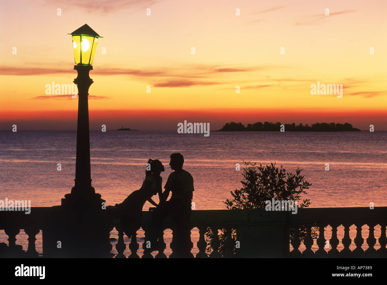 Paar auf Wand bei Sonnenuntergang unter Lampe in Colonia del Sacramento in Uruguay Stockfoto