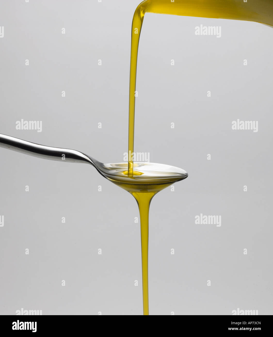 Natives Olivenöl extra, das über einen Löffel auf einem neutralen Hintergrund gegossen wird Stockfoto