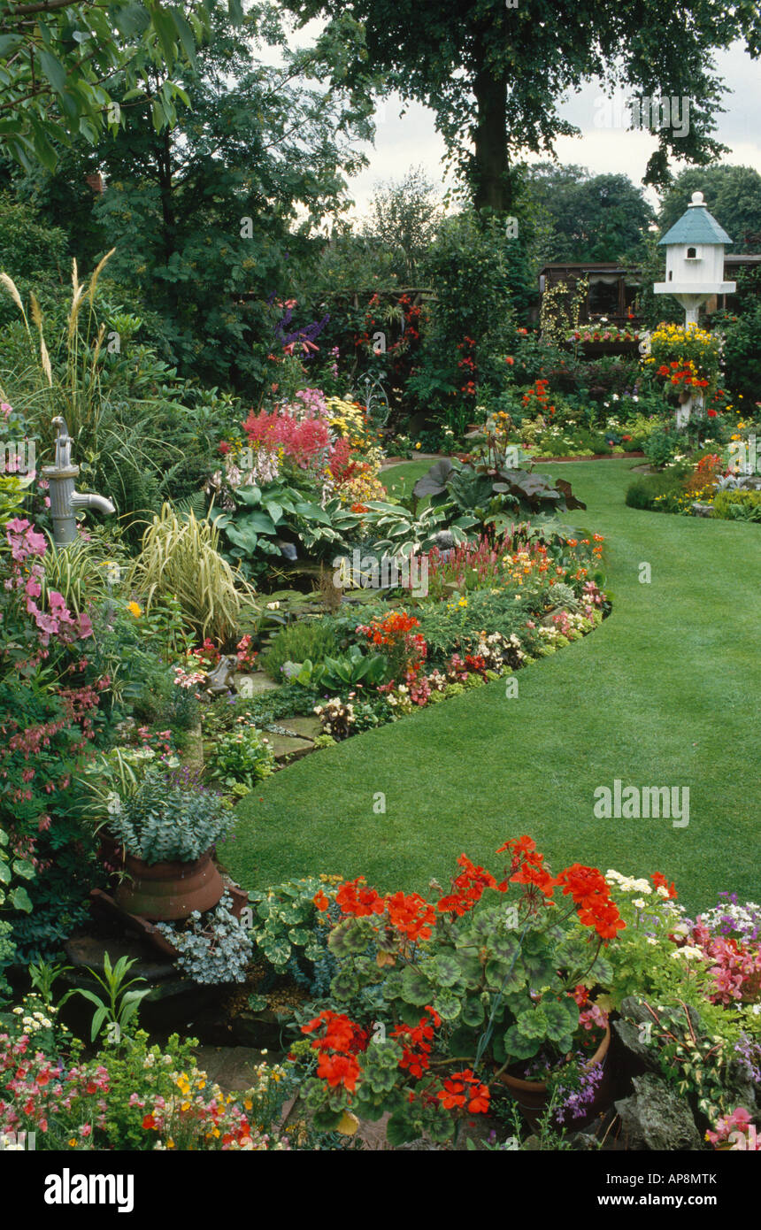 Rote Geranien und bunte Sommerblumen in s Garten mit Vogelhaus und gebogene Rasen Stockfoto