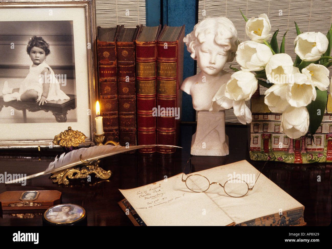 Wohneinrichtungen. Bibliothek. Altmodische Hausbibliothek. Bücher, weiße Blumen, ein altes Foto eines Kindes, Kerzenlicht, Erinnerungsstücke und Erinnerungen. Stockfoto