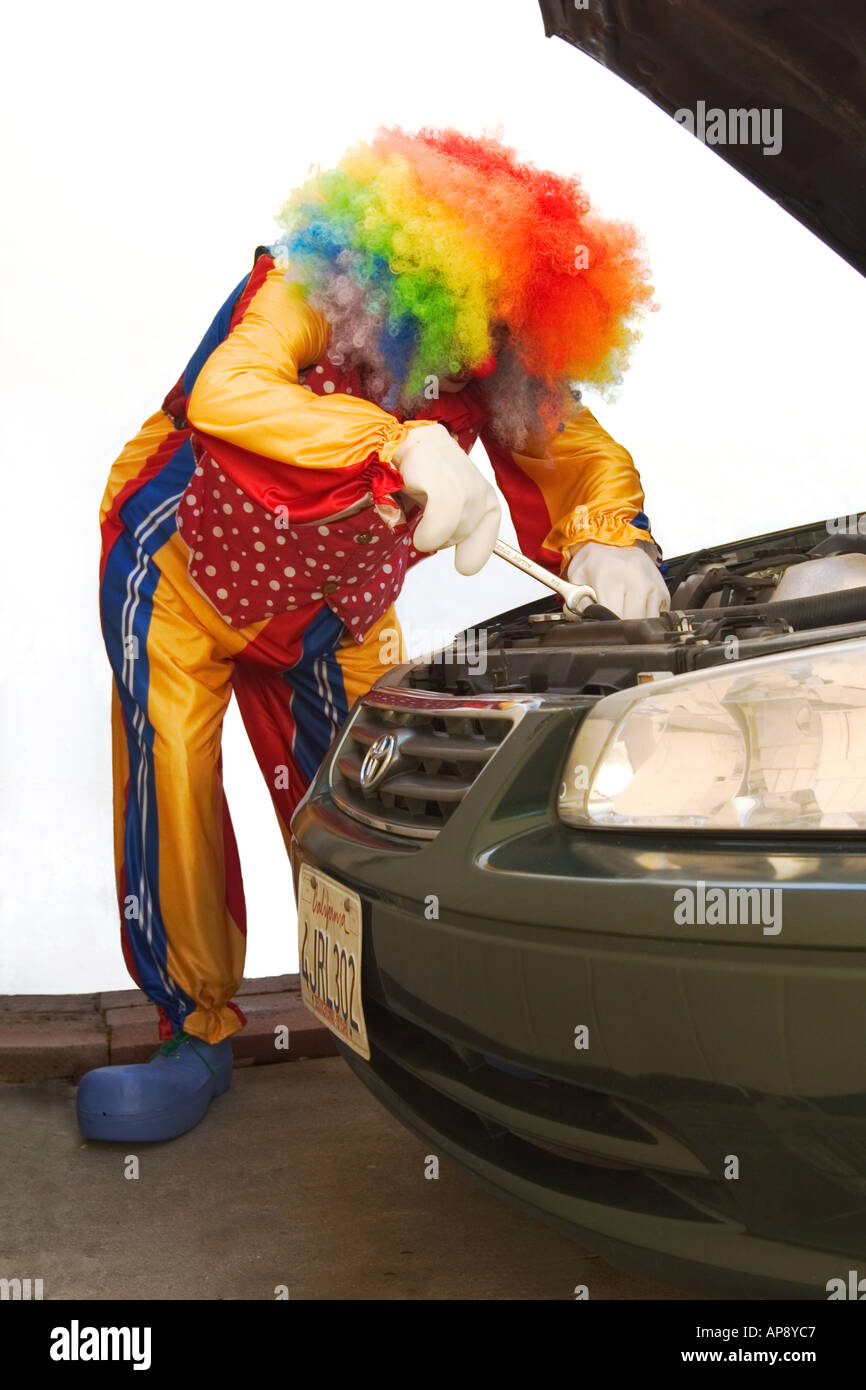 Ein Clown mit bunten Haaren, die Arbeiten am Motor eines Autos. Stockfoto