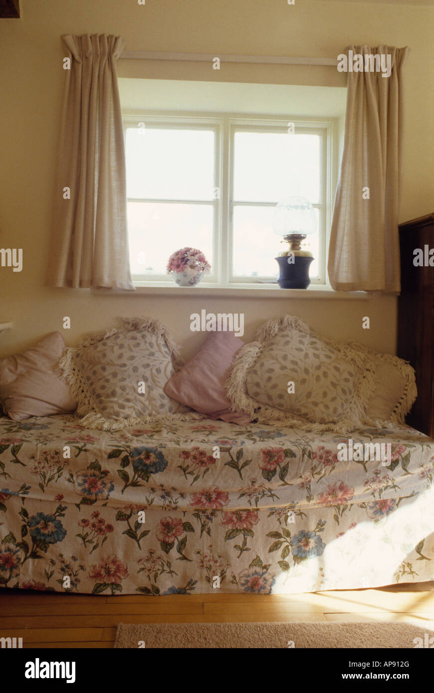 Kissen auf der Couch mit floralen Loosecover unter Fenster mit cremefarbenen Vorhängen im Haus lebenden rooom Stockfoto
