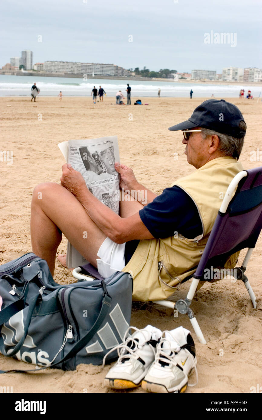 ein Alter senior Mann Lesen einer Zeitschrift oder Zeitung auf einem Liegestuhl in Frankreich-Küste Stockfoto