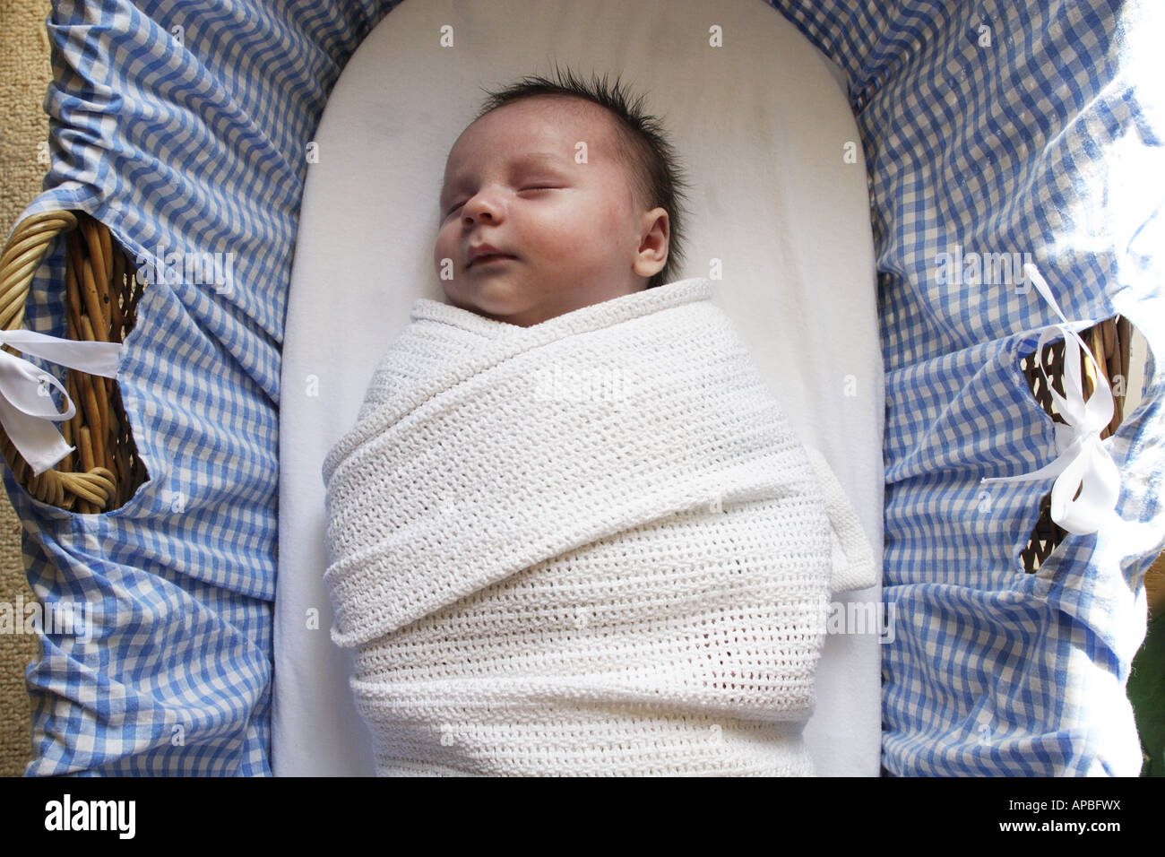 Ein neugeborenes Baby schläft beschützend in eine Decke in einem Körbchen. Stockfoto