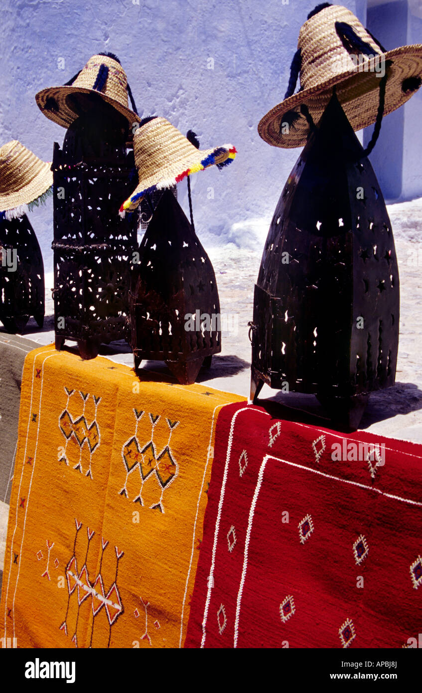 Farbenfrohe Teppiche, traditionelle Hüte und dekorative Kerzenständer in Chefchaouen, Marokko, vor einer blau getünchten Wand. Stockfoto Farbenfrohe Teppiche, traditionelle Hüte und dekorative Kerzenständer in Chefchaouen, Marokko, vor einer blau getünchten Wand. Stockfoto