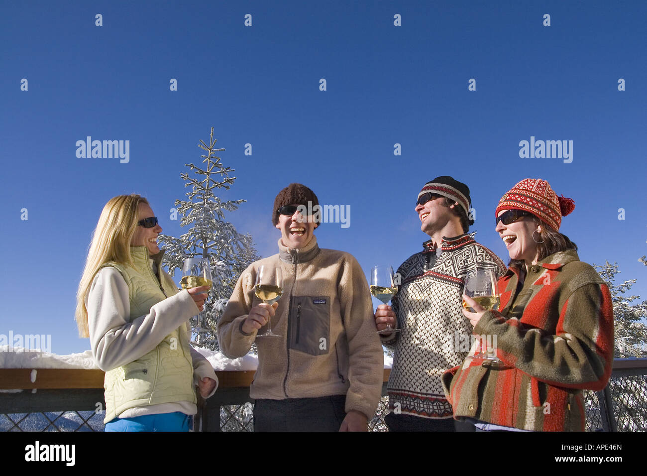 Vier Freunde genießen Weißwein auf dem Deck eines Ski lodge an einem verschneiten Tag während des Gesprächs im Northstar in der Nähe von Lake Tahoe. Stockfoto