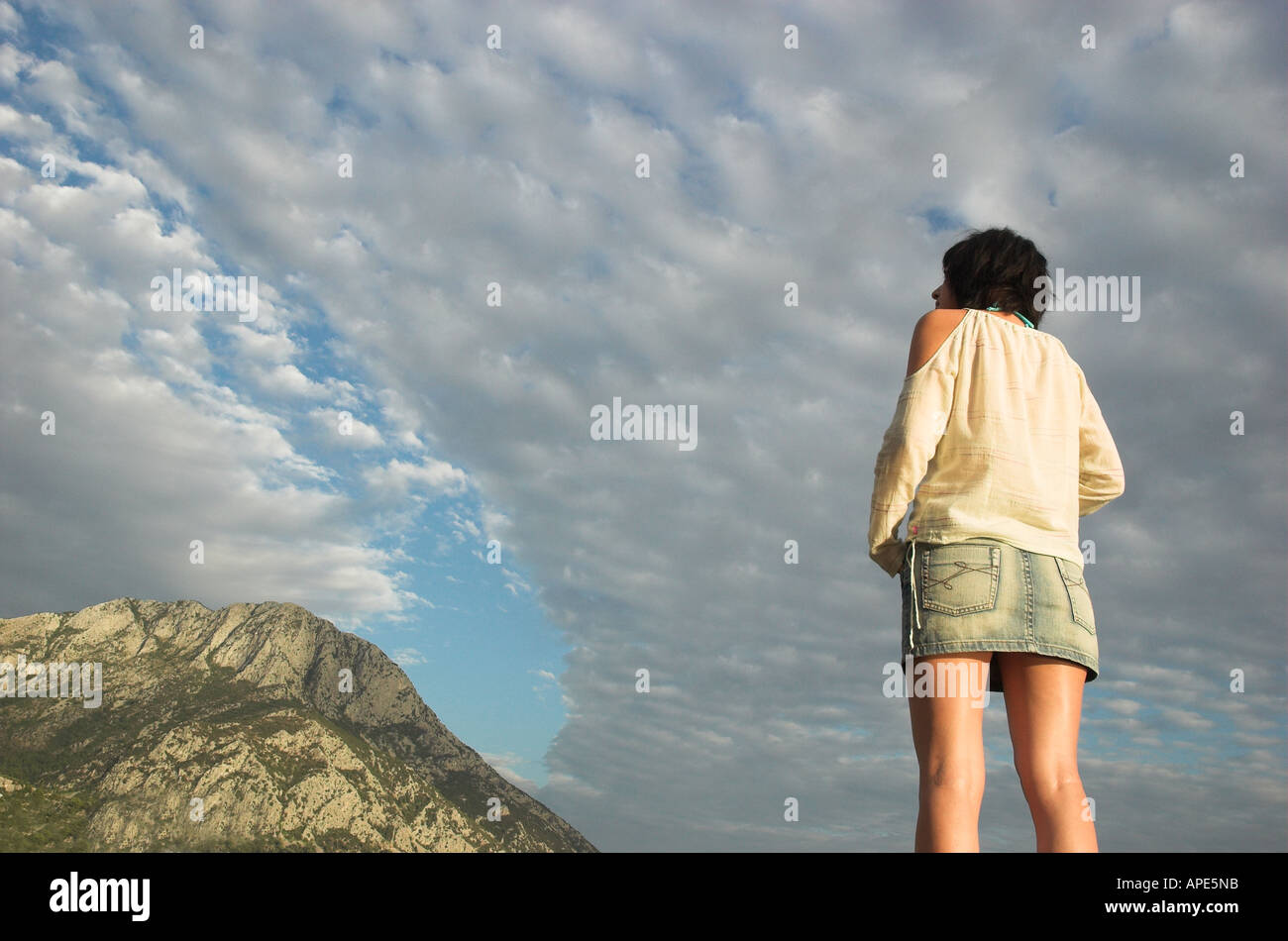 Junge Frau trägt Freizeitkleidung stehen im Freien Schuss gegen bewölktem Himmel warmen weichen Farben, Rückansicht Stockfoto