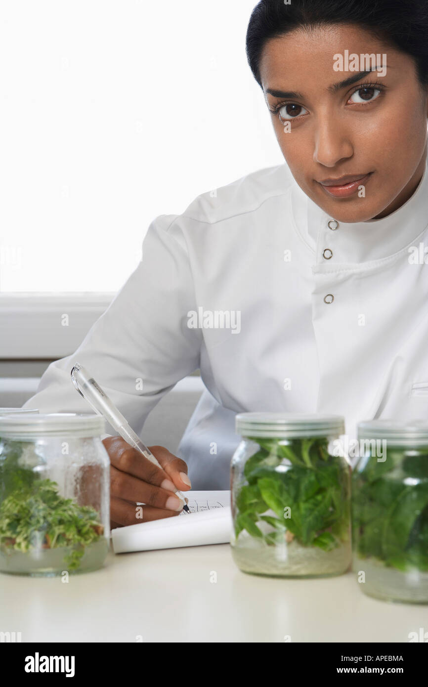 Weibliche Lab Arbeiter mit Glas Gläser mit Pflanzenmaterial, Aufzeichnung von Beobachtungen Stockfoto