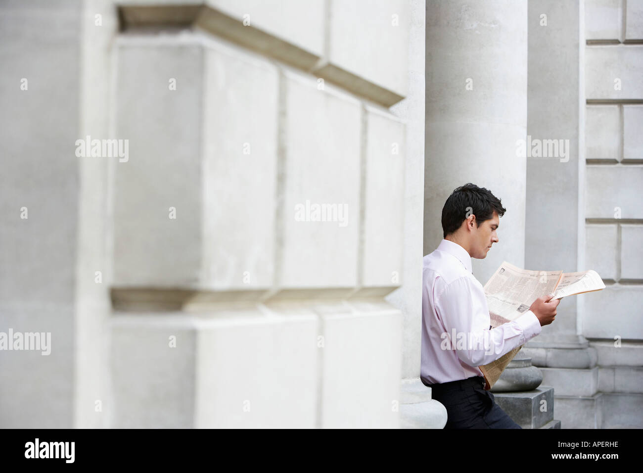Geschäftsmann, sitzen auf Säule lesen Zeitung außerhalb Gebäude Stockfoto