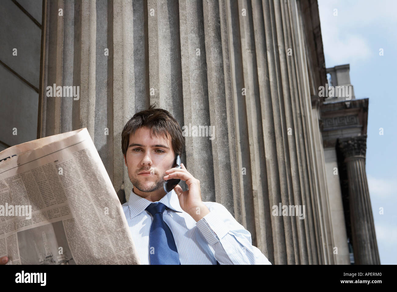 Geschäftsmann lesen Zeitung und Talking auf Handy außerhalb Gebäude Stockfoto