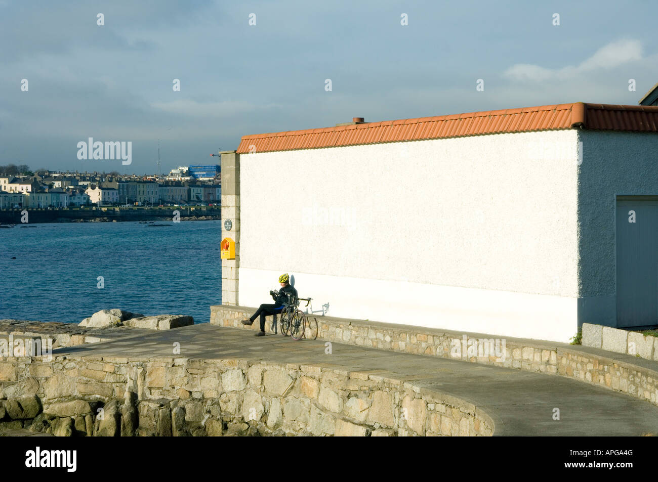 Ein einsamer Radfahrer genießt eine Pause an einer sonnigen Wand neben dem Strand bei Sandycove Dublin Ireland Stockfoto