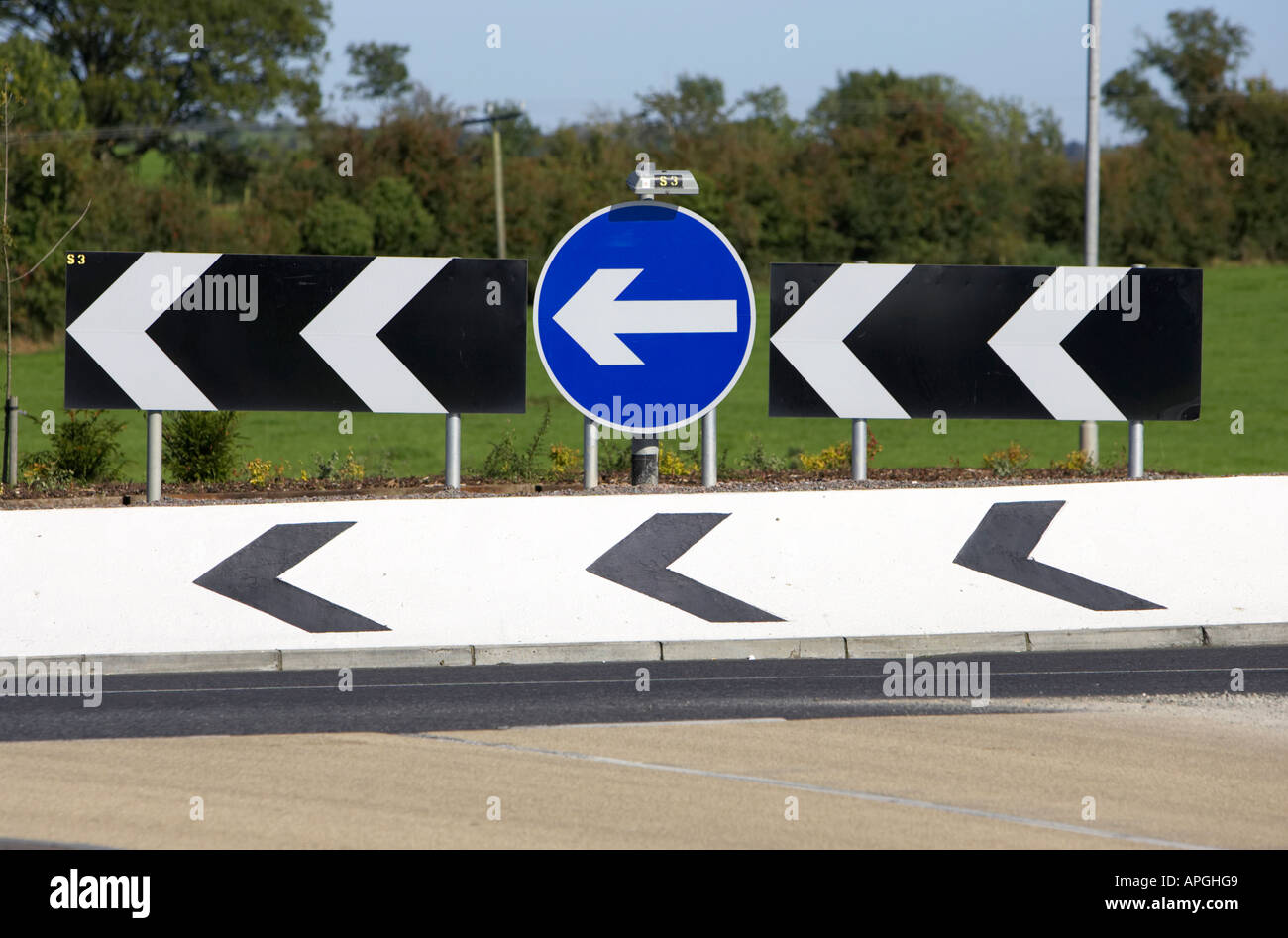 schwarze und weiße scharfe Abweichung zur linken und blaue und weiße Runde linke Straße Zeichen in der Mitte eines Kreisverkehrs Stockfoto